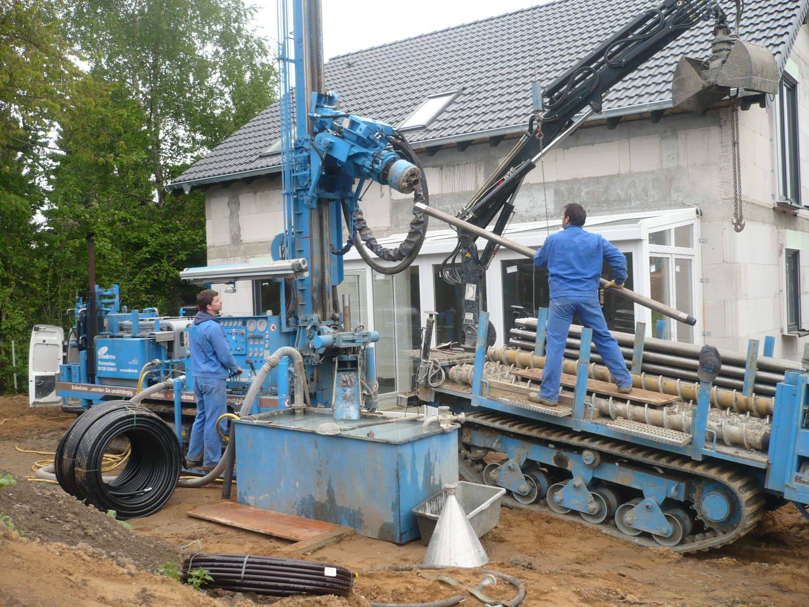 Bohrgerät setzt eine Erdwärmesonde neben einem Einfamilienhaus